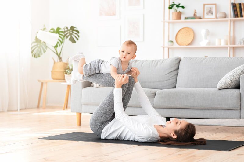 Frau auf Yogamatte in Rückenlage macht Sport mit Baby