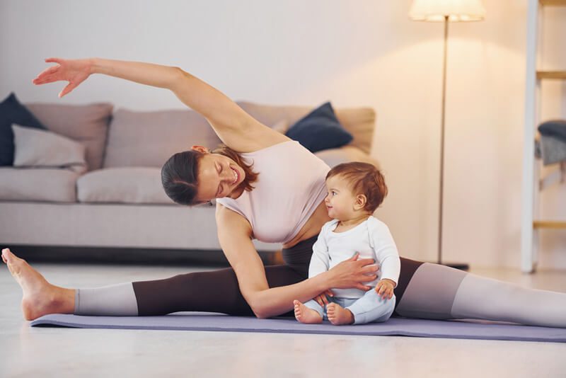 Frau in Yogapose mit Baby vor ihrem Schoß