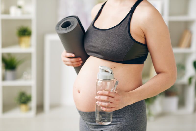 Schwangere Frau auf dem Weg zum Yogakurs mit Yogamatte und Getränk